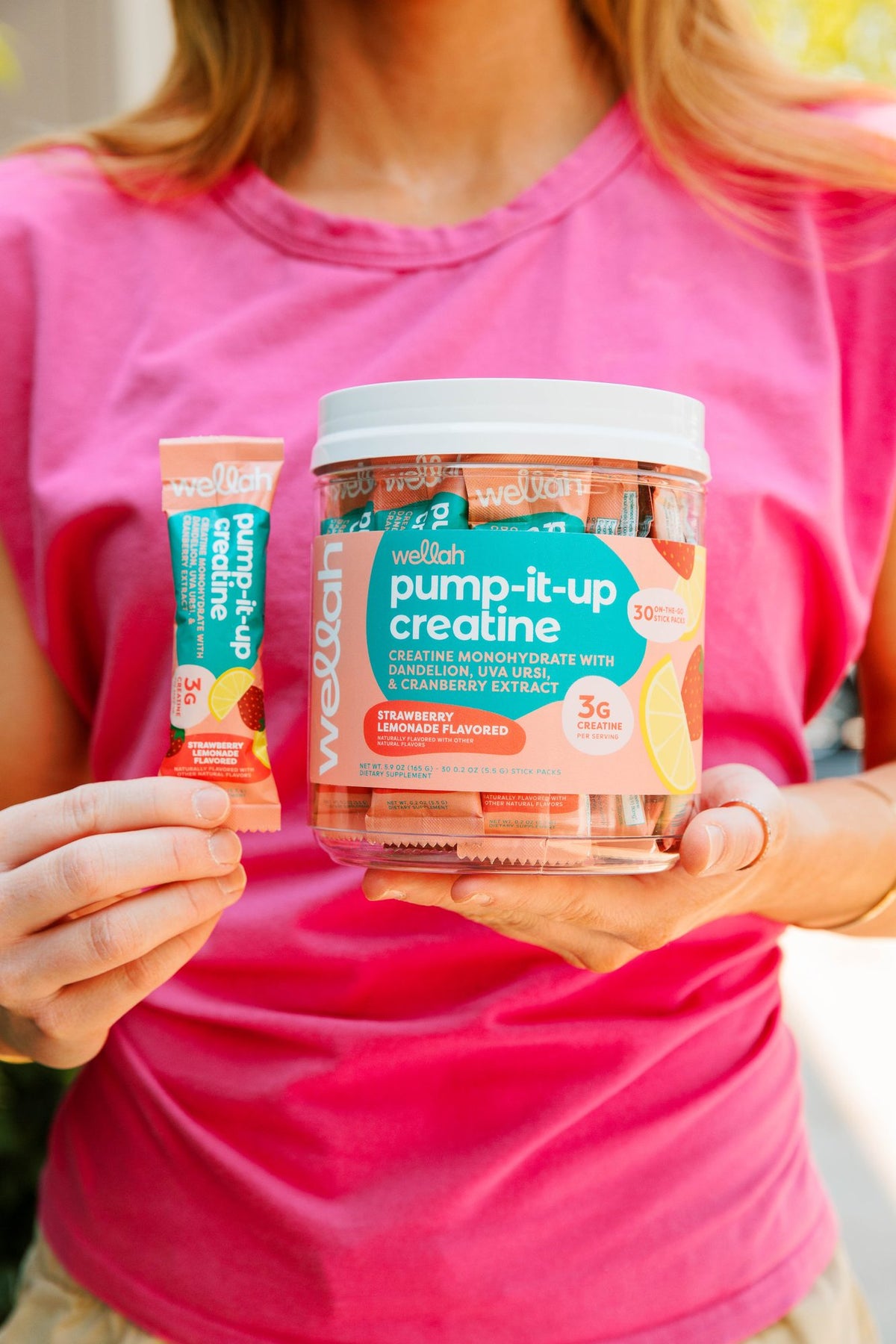 Woman holding a Wellah creatine stick pack and tub